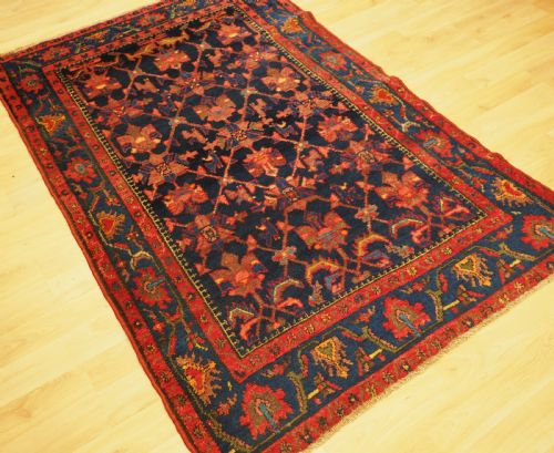 fig 1. An antique hand-knotted Persian rug featuring a deep navy blue field with a red floral lattice pattern surrounded by a broad patterned border.