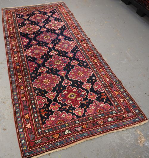 fig 1. An antique long Caucasian runner rug featuring repeating pink and yellow geometric medallions on a dark navy field surrounded by a multi-band decorative border.