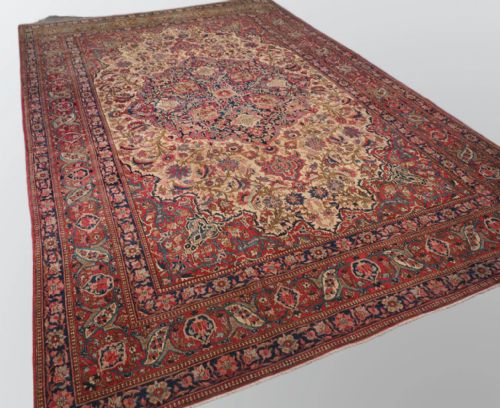 fig 1. An antique rectangular Isfahan carpet featuring a detailed central medallion, cream field with red and blue floral arabesques, and a decorative multi-banded border.