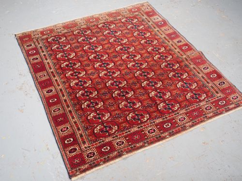 fig 1. A rectangular hand-knotted Tekke Turkmen wool rug featuring repeated geometric primary guls on a deep red field surrounded by multi-band borders.