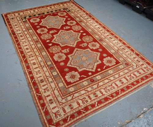 fig 1. An antique East Turkestan Khotan wool area rug featuring three light blue geometric star medallions on a red field within wide cream and beige patterned borders.