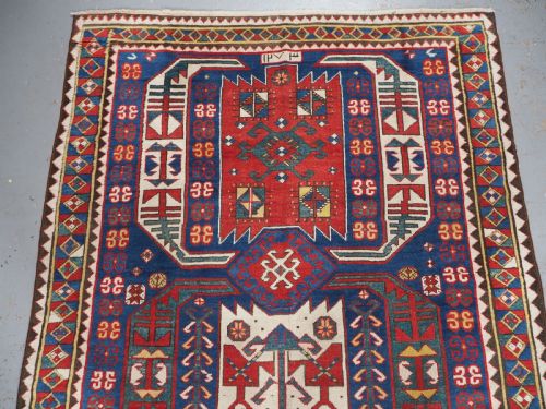 fig 2. An antique hand-knotted Caucasian Kasim-Usag wool rug featuring geometric red and ivory medallions set on a dark navy blue field with multi-coloured geometric borders.