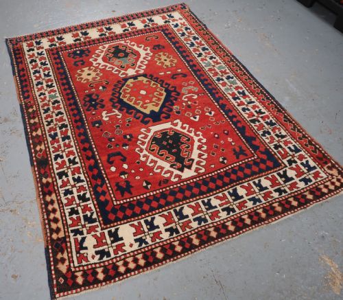 fig 1. An antique Caucasian Bordjalou Kazak hand-knotted wool rug featuring three stepped geometric medallions on a vibrant red field within patterned borders.