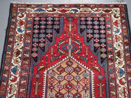 fig 2. An antique hand-knotted Persian Mazlaghan wool rug featuring a central camel-coloured medallion on a red stepped field with dark blue rosette borders.