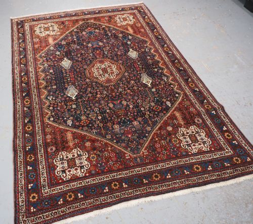 fig 1. A rectangular hand-knotted antique Abadeh rug featuring a navy blue central field with a diamond medallion and rust red geometric spandrels.