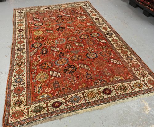 fig 1. An antique South Persian Shekarlu Qashqai wool rug featuring a red field with dense geometric tribal motifs surrounded by an ivory patterned border.