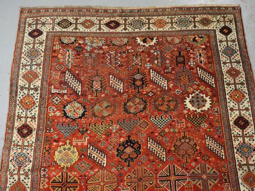 fig 2. An antique South Persian Shekarlu Qashqai wool rug featuring a red field with dense geometric tribal motifs surrounded by an ivory patterned border.
