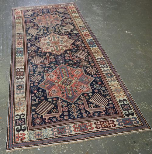 fig 1. An antique Caucasian Akstafa long rug runner featuring three star medallions and stylized peacock motifs on a dark navy blue field with geometric borders.