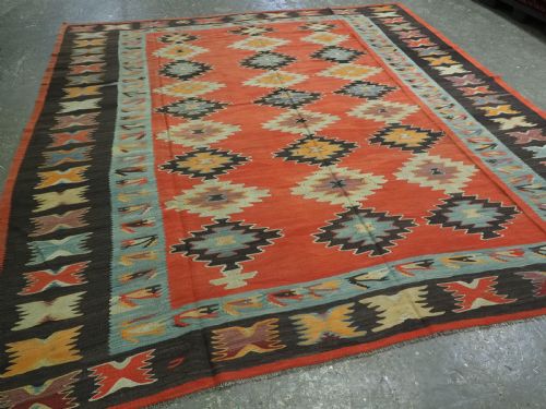 fig 1. A large antique Pirot Sarkoy flat-weave wool kilim carpet featuring repeating diamond medallions on a terracotta field with dark geometric borders.
