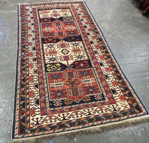 fig 1. An antique hand-knotted Caucasian Shirvan wool rug featuring geometric stepped medallions on a deep blue field with red and cream patterned borders.