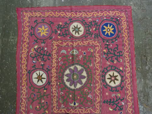 fig 1. A rectangular hand-embroidered pink silk on cotton suzani textile featuring circular floral motifs, star shapes, and scrolling vine borders.