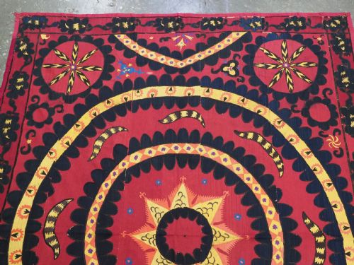 fig 1. A rectangular crimson Uzbek suzani textile featuring heavy silk embroidery with a central star motif inside concentric circular borders.