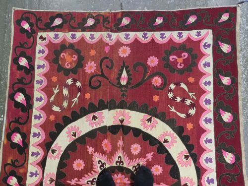 fig 1. A rectangular hand-embroidered textile featuring a large central circular starburst medallion surrounded by floral motifs in shades of pink, cream, orange, and burgundy.