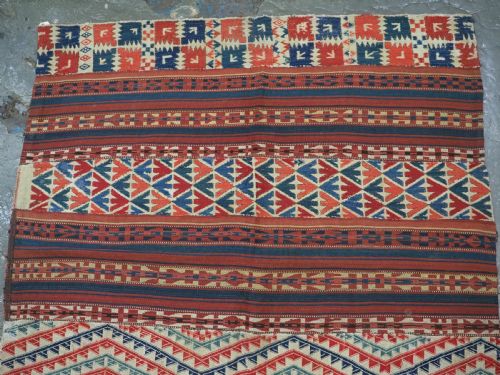 fig 1. An antique central Asian kilim rug composed of thirteen vertical strips showing geometric diamond and stripe patterns in red, navy blue, and cream.