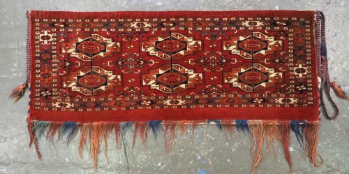 fig 1. A horizontal handwoven wool Tekke Turkmen torba featuring six octagonal gul medallions on a deep red background with geometric borders and braided side tassels.