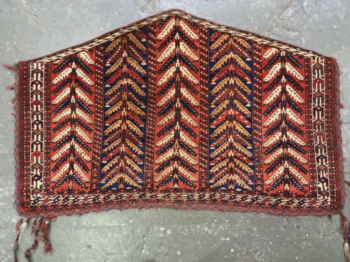 fig 1. A pentagonal antique Turkmen wool textile featuring vertical rows of white and gold chevron leaf motifs on a dark red background framed by geometric borders.