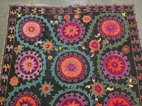 fig 1. An antique Uzbek suzani textile featuring vibrant purple, orange, and teal silk embroidery in medallion patterns across a black cotton ground.