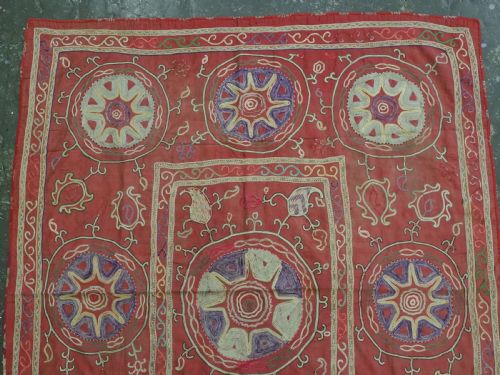 fig 1. A rectangular red cotton embroidered suzani featuring geometric starburst medallions and floral scrolling borders worked in multi-coloured silk thread.