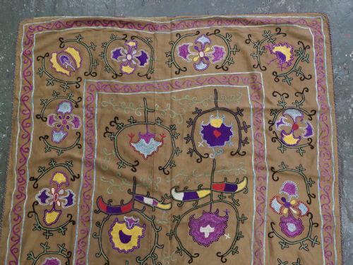 fig 1. An antique Uzbek Nim Suzani textile featuring hand-embroidered floral motifs and hooked borders in purple, yellow, and blue silk threads on a tan cotton ground.