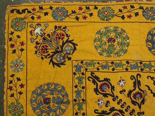 fig 1. A rectangular yellow cotton textile featuring hand-embroidered silk floral medallions, vines, and circular motifs in blue, green, and burgundy.