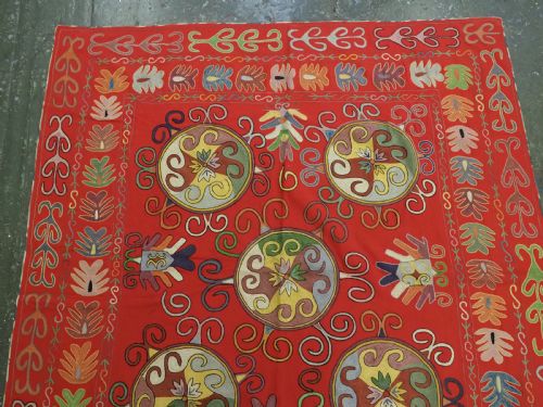 fig 1. A rectangular red wool textile featuring multi-coloured silk embroidery with central circular medallions and decorative botanical borders.