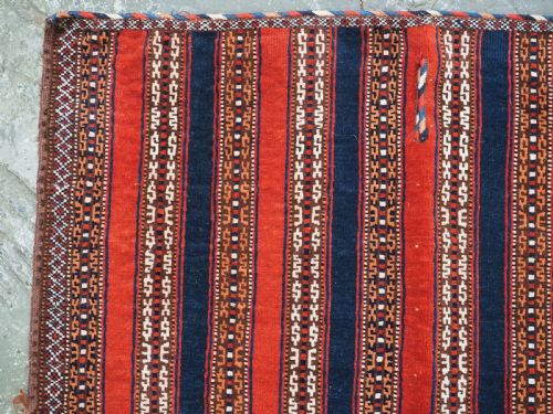 fig 1. An antique square Turkmen Yomut saddle rug featuring vertical red and navy blue stripes with geometric tribal patterns and woven borders.