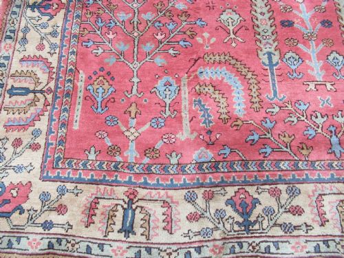 fig 1. An antique Turkish Oushak wool carpet featuring a dominant pink ground decorated with stylized willow tree motifs and framed by a light beige floral border.