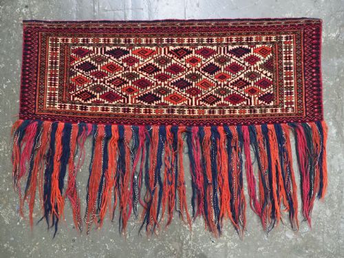 fig 1. An antique rectangular Tekke Turkmen woven torba face featuring a geometric diamond lattice pattern in burgundy, cream, and orange, finished with long polychrome wool fringes along the lower edge.