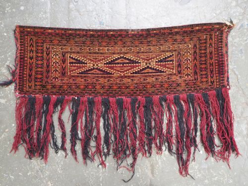 fig 1. An antique woven Tekke Turkmen torba featuring intricate geometric lattice motifs in dark red, terracotta, and dark blue with a long braided fringe along the bottom edge.