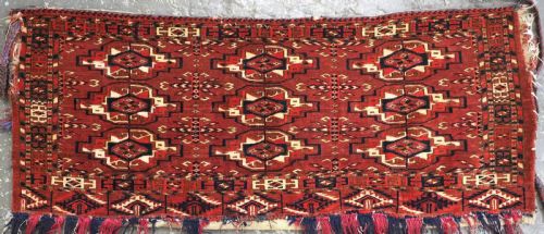 fig 1. A horizontal rectangular handwoven wool Tekke Turkmen torba bag featuring nine geometric gul motifs in red, navy, and ivory, complete with a long hanging wool fringe at the base.