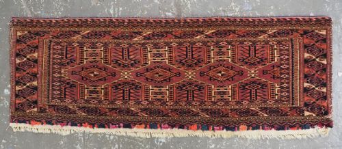 fig 1. An antique rectangular hand-knotted wool Saryk Turkmen torba face displaying geometric diamond medallions in red, terracotta, and navy shades with lower fringe detail.