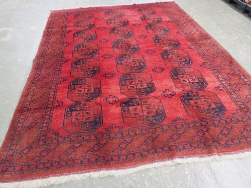 fig 1. A hand-knotted antique Afghan wool carpet in warm red featuring dark blue repeating octagonal gul motifs and geometric borders.