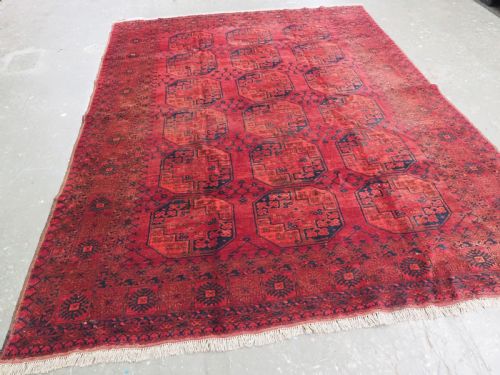 fig 1. An antique hand-knotted Afghan Ersari wool carpet featuring dark blue octagonal gul motifs arranged in rows on a warm red field.