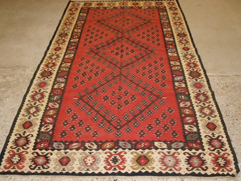 OLD TURKISH SARKOY KILIM RUG, TRADITIONAL DESIGN ON SOFT RED GROUND, GOOD IVORY BORDER, CIRCA 1920.