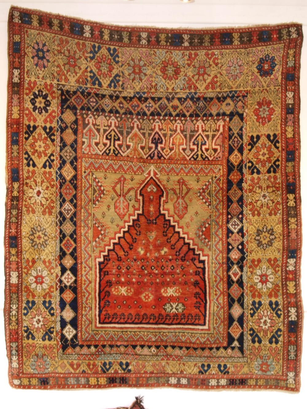 An antique mid-19th century Turkish Mujur prayer rug featuring a central terracotta stepped mihrab niche framed by intricate multi-coloured geometric borders.