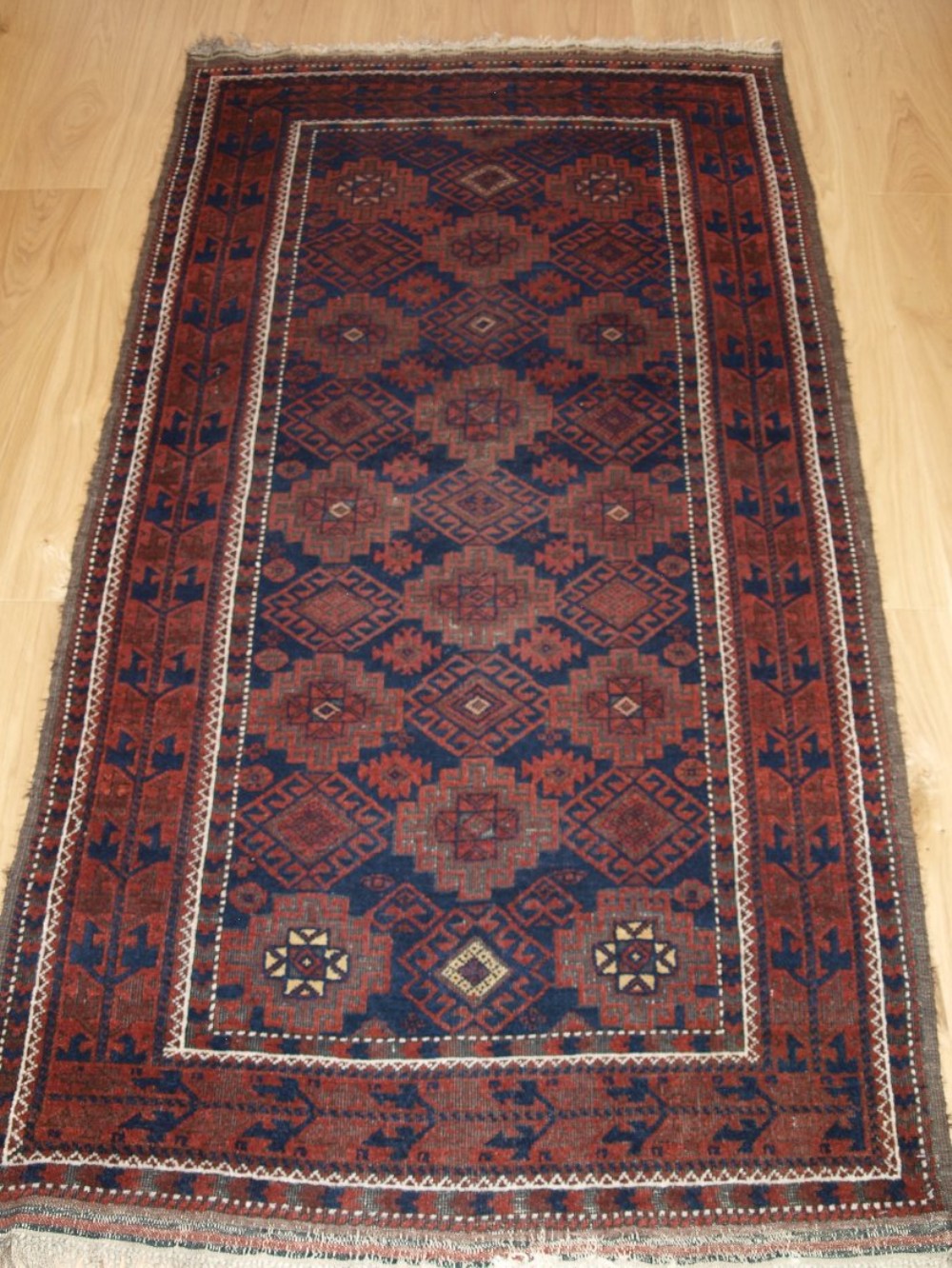 ANTIQUE BALUCH RUG WITH REPEAT DESIGN, HEAVY CORROSION, CIRCA 1900.