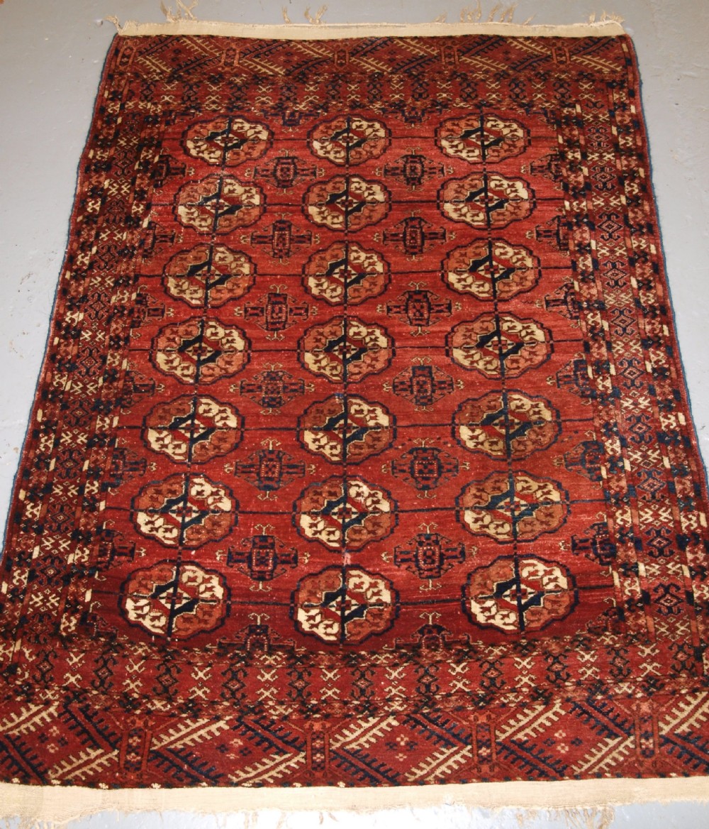 An antique late 19th-century Tekke Turkmen wool rug featuring rows of octagonal gul medallions on a deep red ground with geometric borders.