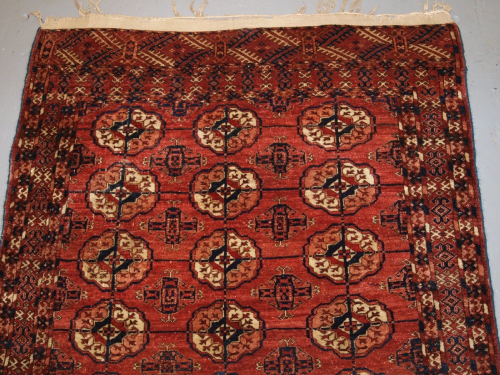 An antique late 19th-century Tekke Turkmen wool rug featuring rows of octagonal gul medallions on a deep red ground with geometric borders. View II