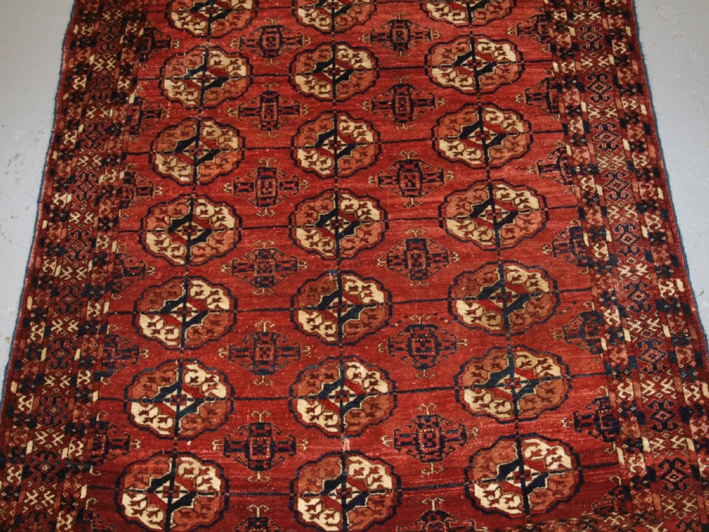 An antique late 19th-century Tekke Turkmen wool rug featuring rows of octagonal gul medallions on a deep red ground with geometric borders. View III