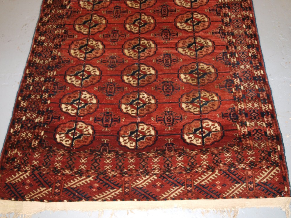 An antique late 19th-century Tekke Turkmen wool rug featuring rows of octagonal gul medallions on a deep red ground with geometric borders. View IV