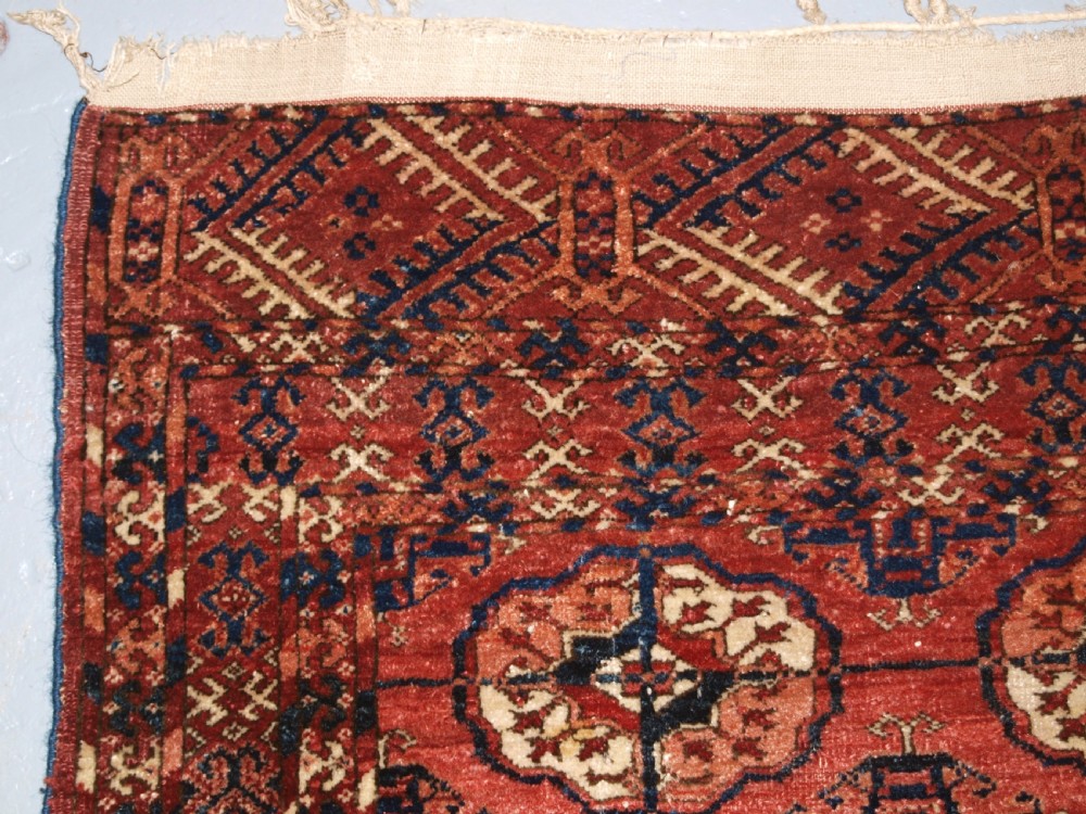 An antique late 19th-century Tekke Turkmen wool rug featuring rows of octagonal gul medallions on a deep red ground with geometric borders. View V