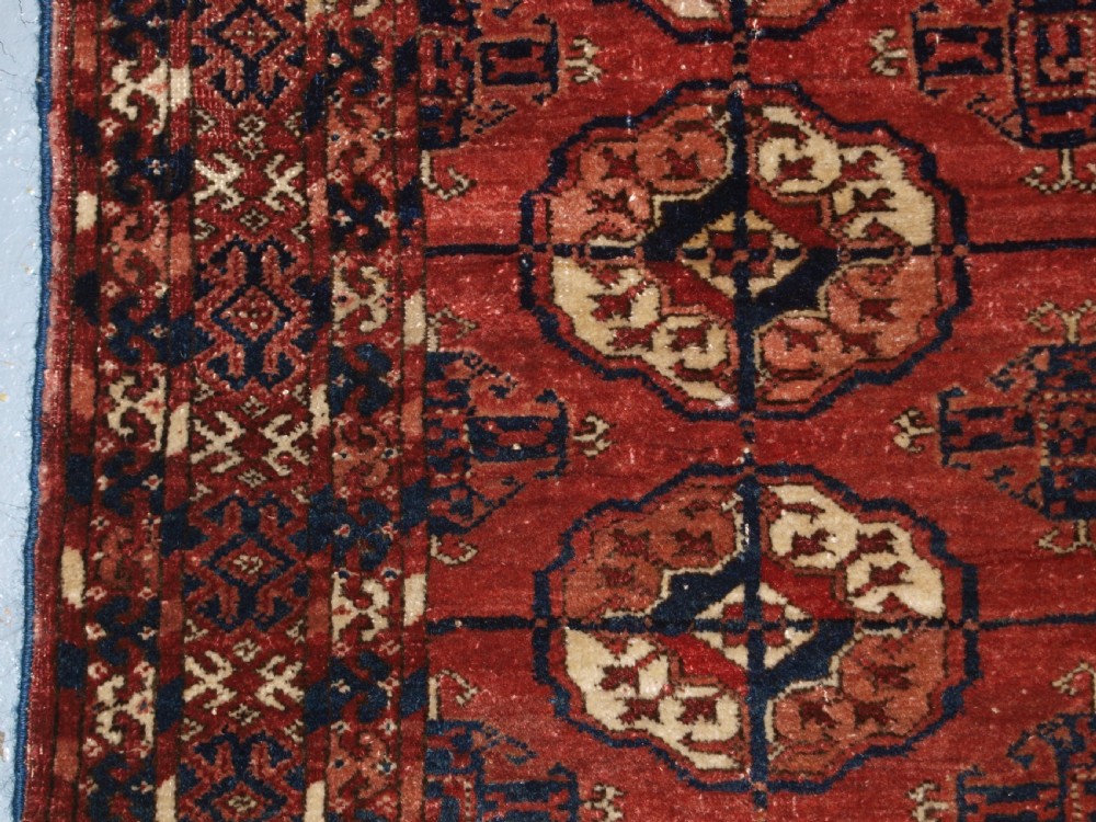 An antique late 19th-century Tekke Turkmen wool rug featuring rows of octagonal gul medallions on a deep red ground with geometric borders. View VI