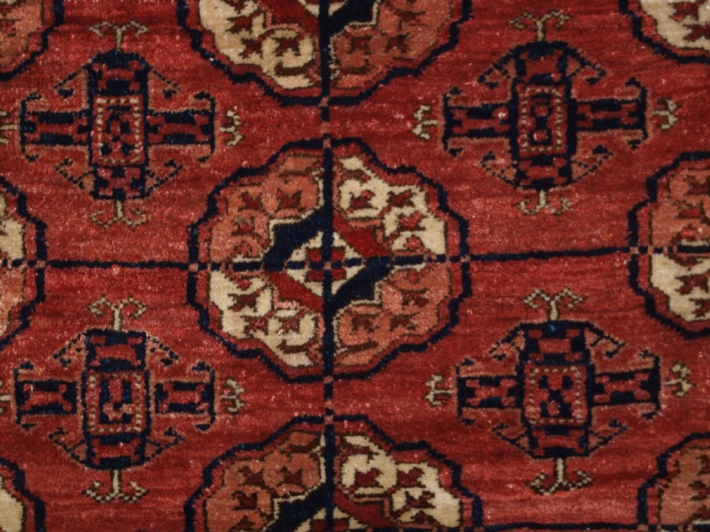 An antique late 19th-century Tekke Turkmen wool rug featuring rows of octagonal gul medallions on a deep red ground with geometric borders. View VII