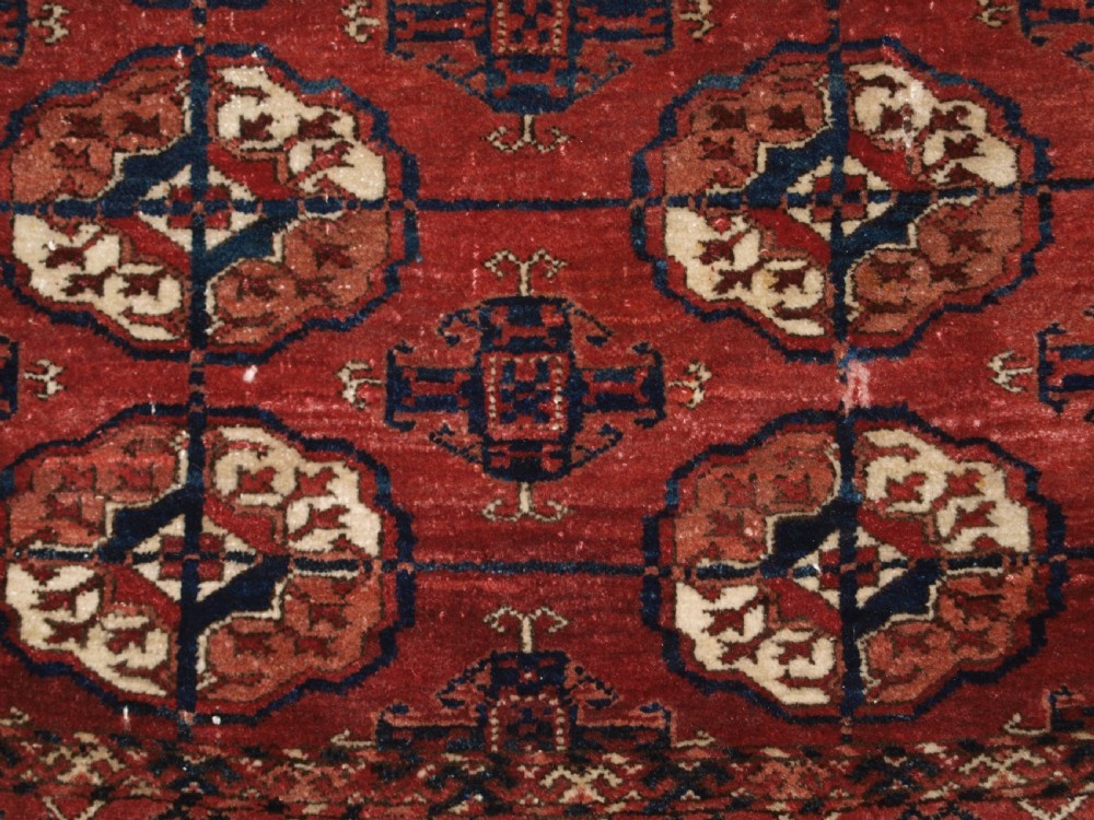 An antique late 19th-century Tekke Turkmen wool rug featuring rows of octagonal gul medallions on a deep red ground with geometric borders. View VIII