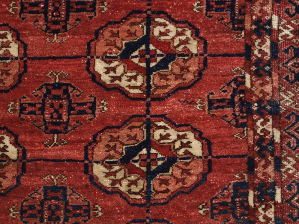 An antique late 19th-century Tekke Turkmen wool rug featuring rows of octagonal gul medallions on a deep red ground with geometric borders. View IX