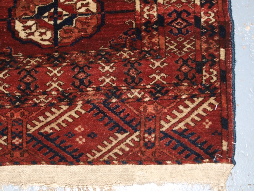 An antique late 19th-century Tekke Turkmen wool rug featuring rows of octagonal gul medallions on a deep red ground with geometric borders. View X