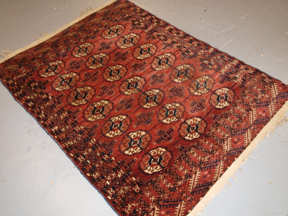 An antique late 19th-century Tekke Turkmen wool rug featuring rows of octagonal gul medallions on a deep red ground with geometric borders. View XI