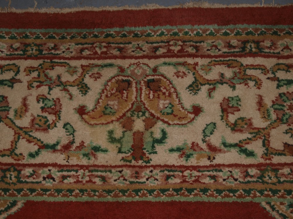 An antique Turkish Isparta wool carpet featuring a warm red field decorated with a central floral medallion and pastel borders. View IX