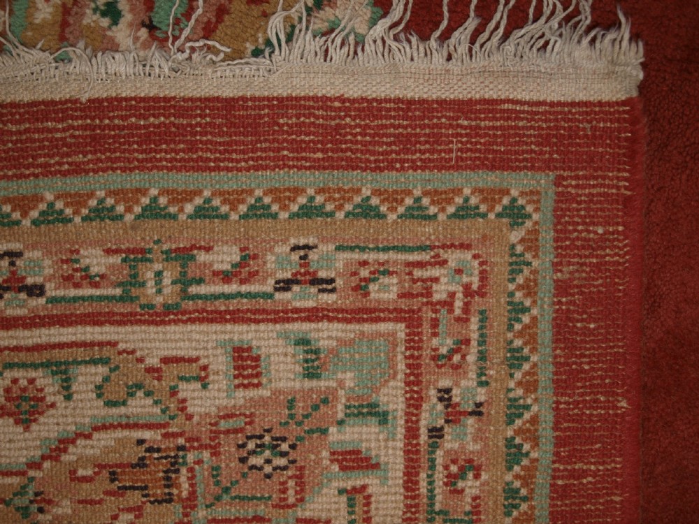 An antique Turkish Isparta wool carpet featuring a warm red field decorated with a central floral medallion and pastel borders. View XIII