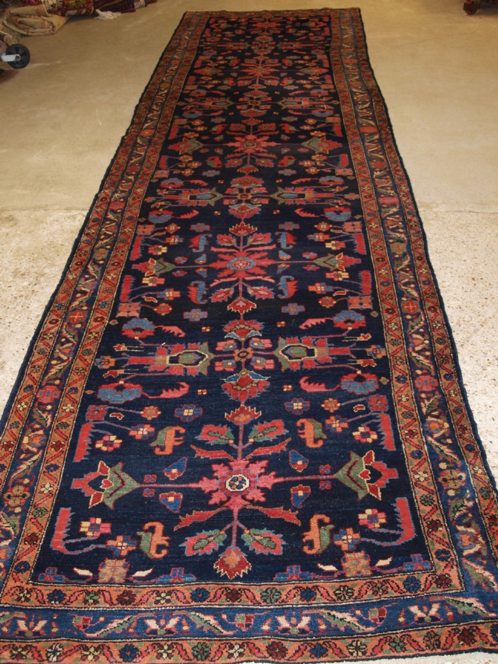 An antique Persian Hamadan wool runner featuring geometric floral patterns in red, green, and blue on a dark navy field surrounded by ornate multi-band borders.